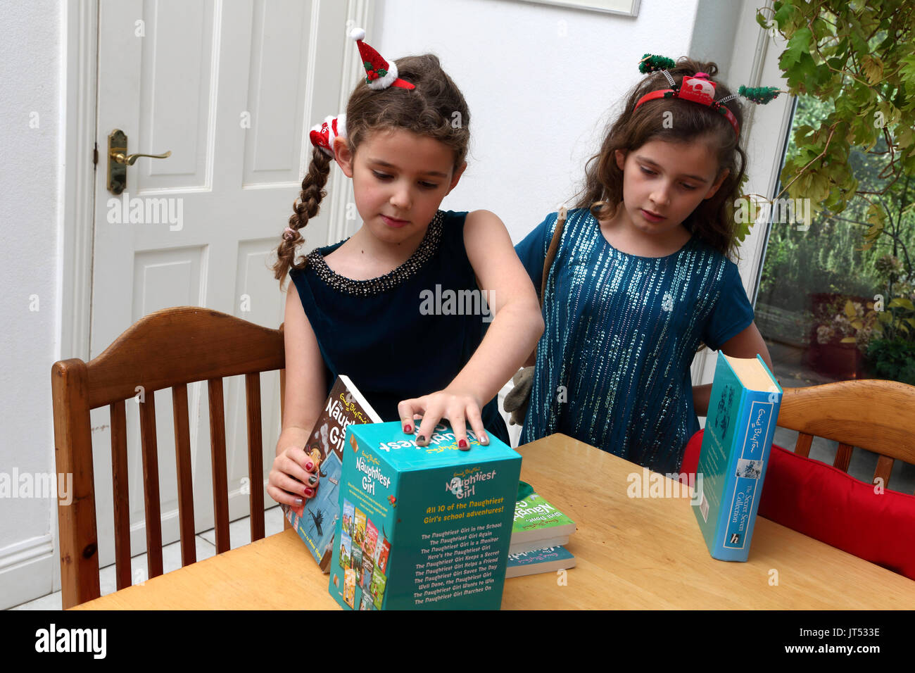 Sorelle al Natale con la festosa alice bande nel loro capelli guardando alla raccolta di Enid Chelmsford libri La ragazza Naughtiest Surrey in Inghilterra Foto Stock