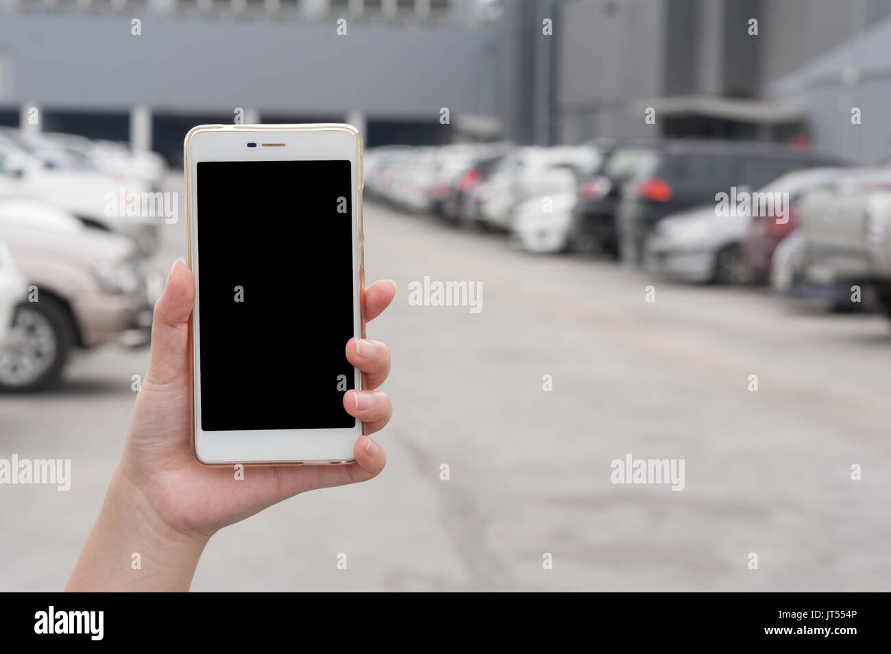 Donna mano azienda smartphone con schermo bianco su sfondo sfocato di area parcheggio per auto. trovare la mia auto utilizzando l'applicazione telefono concept Foto Stock