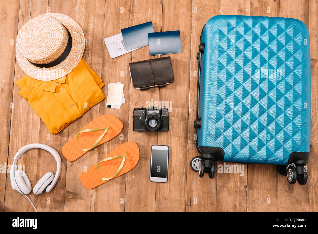 Lay piatto con accessori da viaggio su pavimento di legno. Dispositivi digitali con i vestiti e i passaporti vicino al bagaglio. Foto Stock