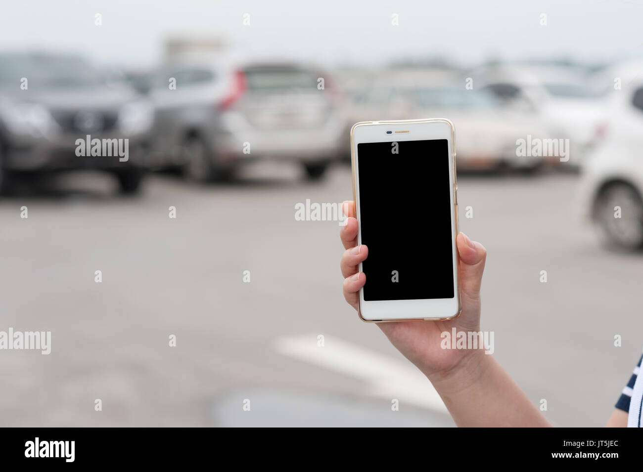 Donna mano azienda smartphone con schermo bianco su sfondo sfocato di area parcheggio per auto. trovare la mia auto utilizzando l'applicazione telefono concept Foto Stock