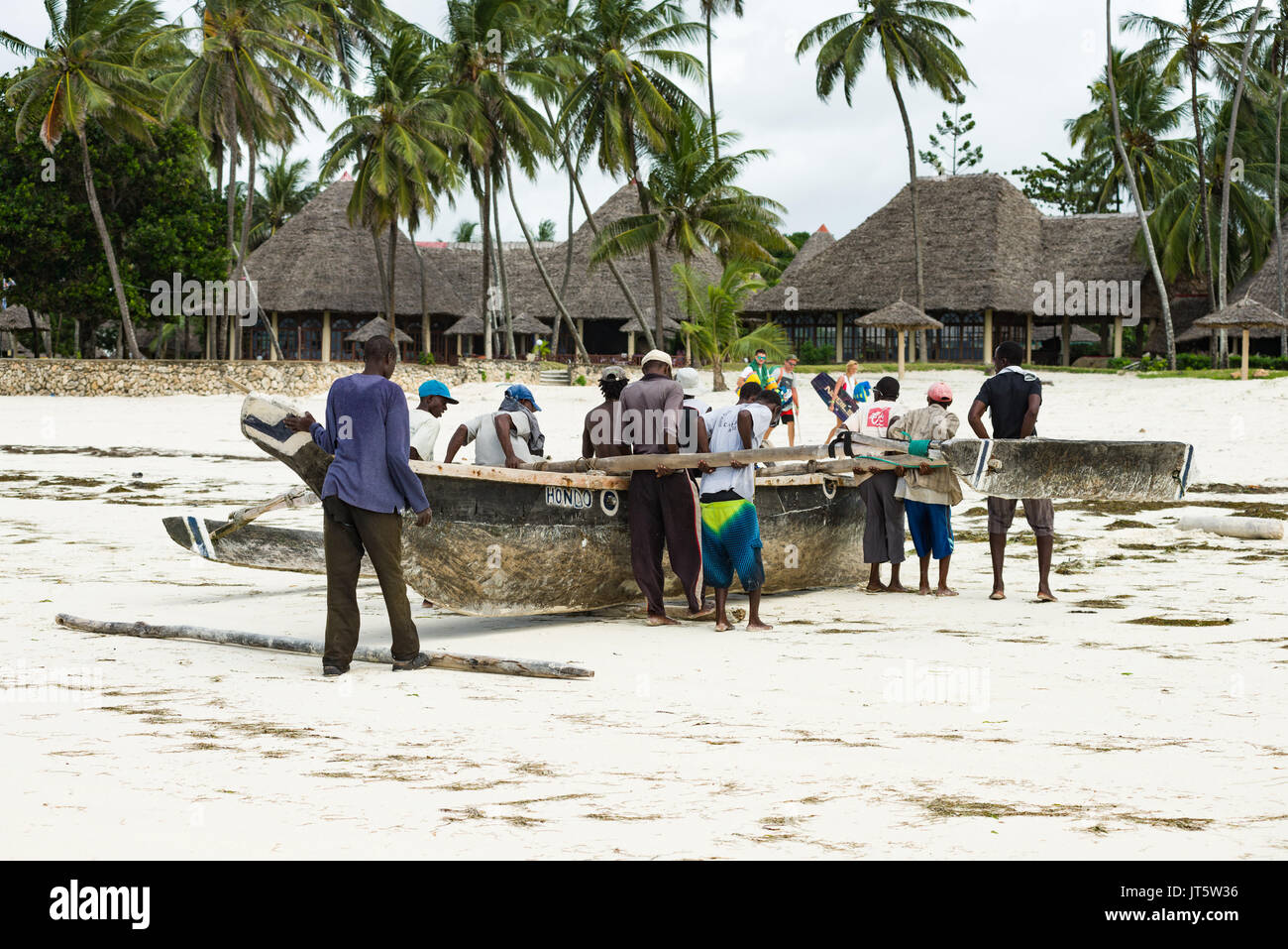 Fisherman spingere sambuco tradizionale barca da pesca lungo la spiaggia e l'oceano, Diani, Kenya Foto Stock