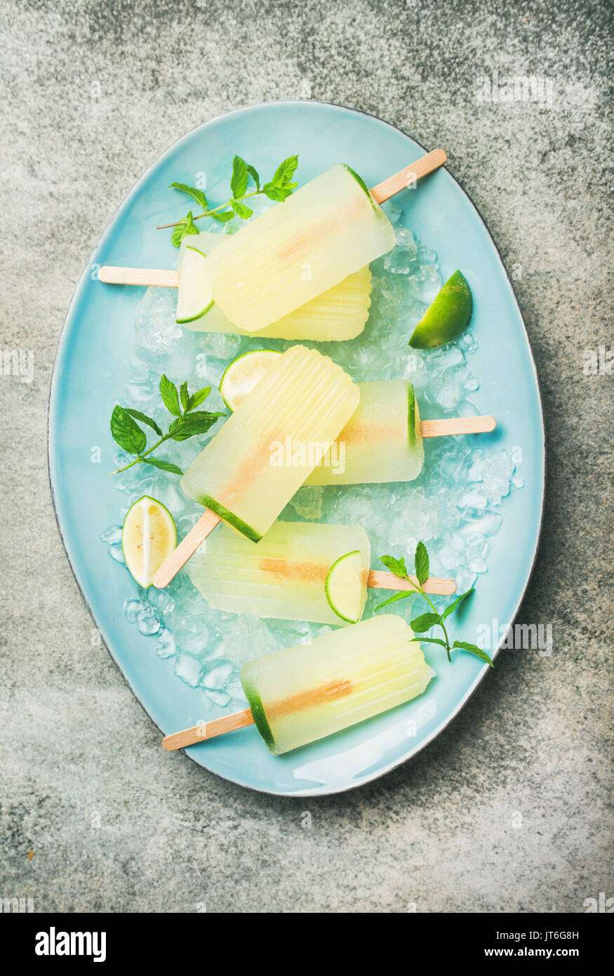 Estate rinfrescante limonata popsicles con lime e menta con scaglie di ghiaccio su piastra blu su sfondo grigio, vista dall'alto Foto Stock