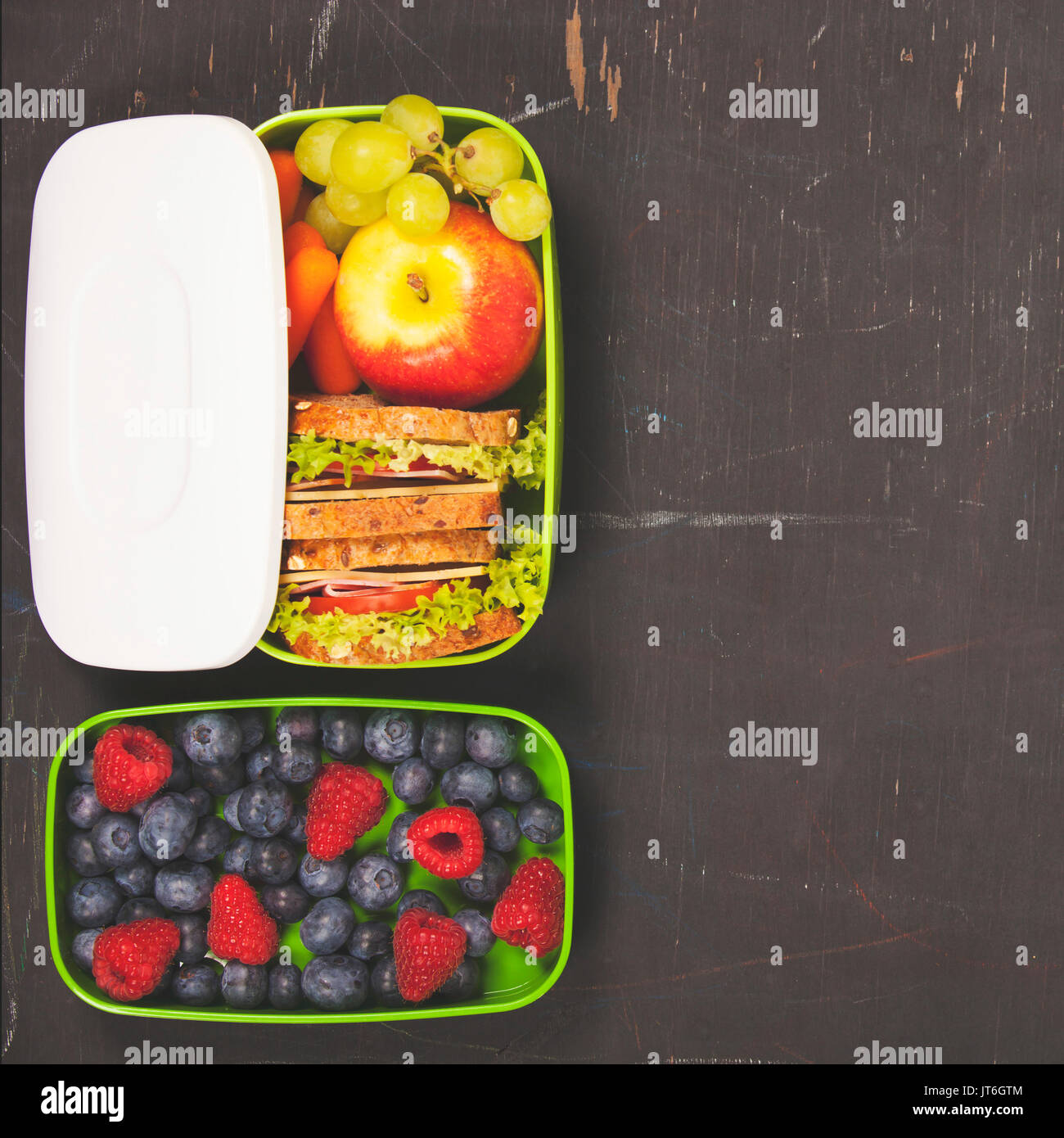 Sandwich, Apple, uva, carota, berry in plastica scatola di pranzo sulla lavagna. Si torna a scuola concetto. Foto Stock
