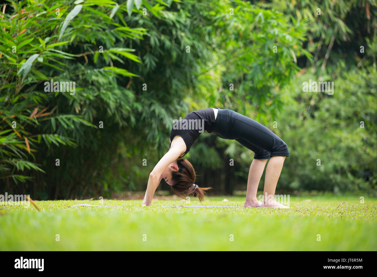 Donna asiatica che indossa abiti neri, la pratica dello yoga in un giardino. Uno stile di vita sano e relax Foto Stock
