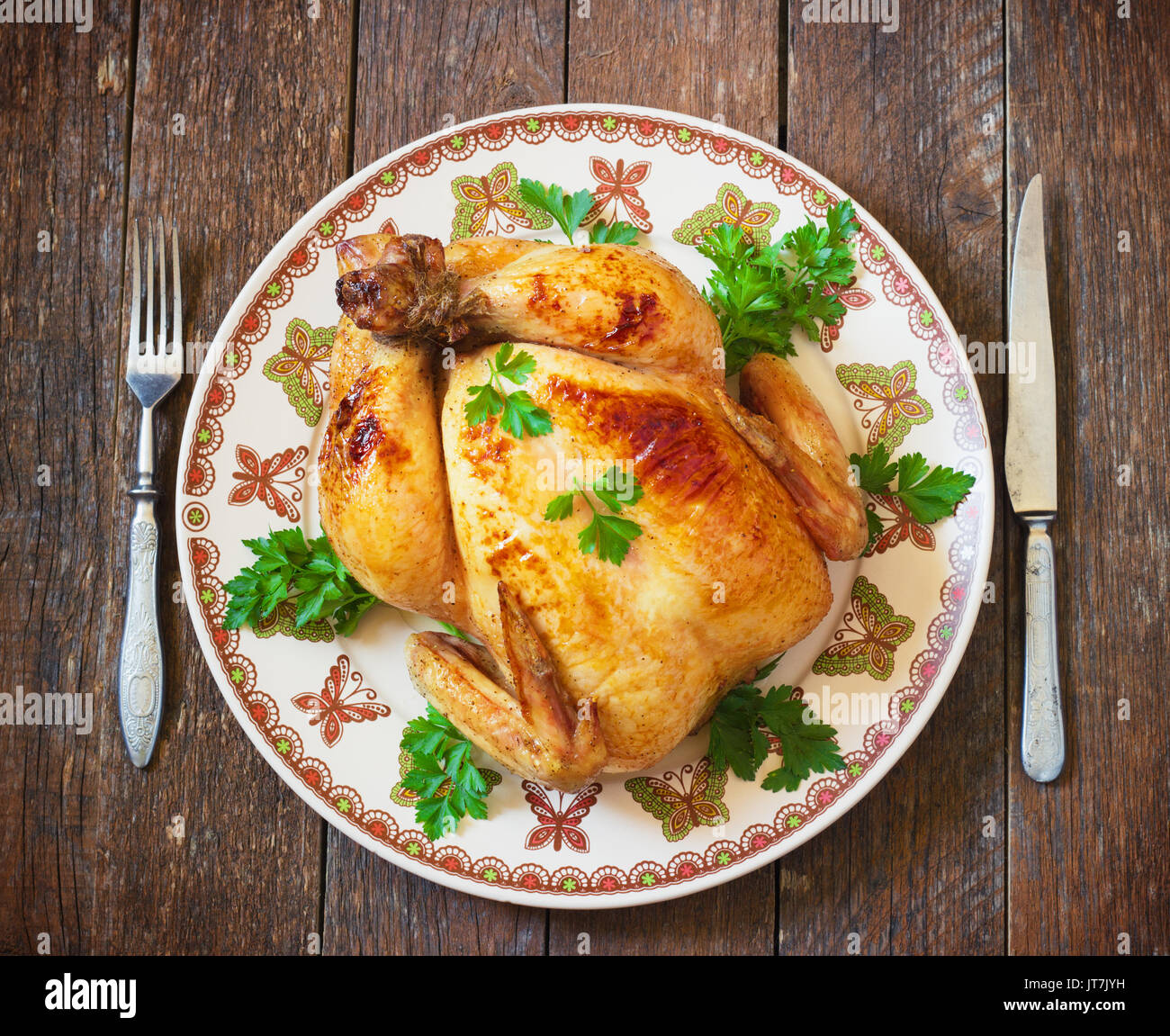 Tutto il pollo arrosto con pomodori e posate su un tavolo di legno tonificante Foto Stock