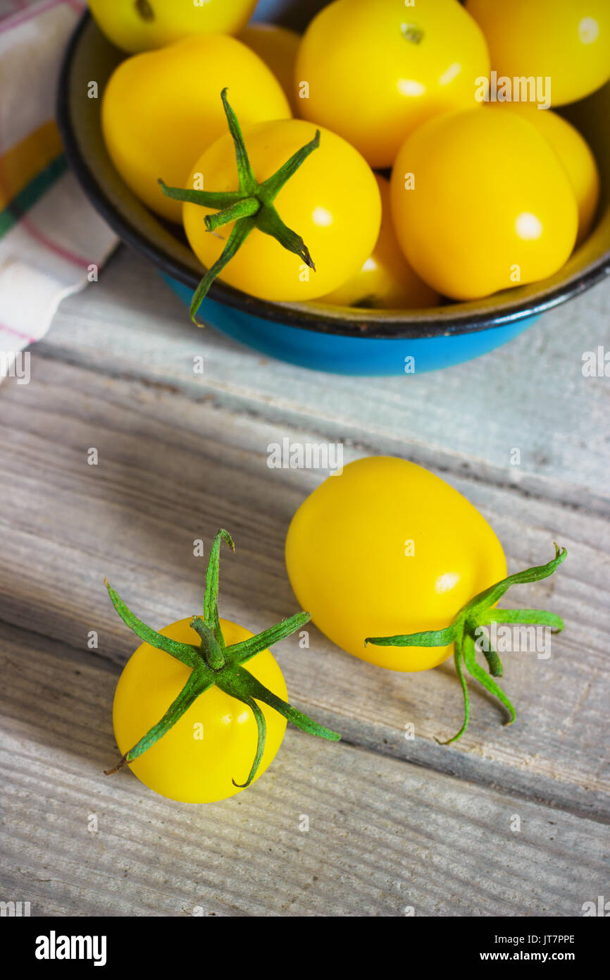 Organico giallo pomodori ciliegia con gocce d'acqua in blu bowlon un tavolo in legno Foto Stock