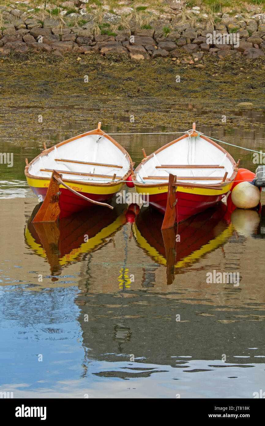 Due vivacemente colorate di rosso, bianco e giallo imbarcazioni a remi / gommoni di fianco a fianco e si riflette nelle calme acque blu del porto di Helmsdale, Scozia Foto Stock