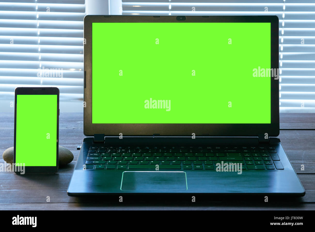 Notebook e smart phone con schermo verde su una scrivania di legno. posto di lavoro mobile Foto Stock