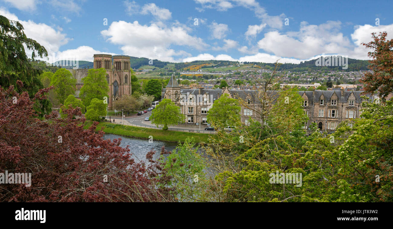 Vista panoramica della città di Inverness con edifici storici e alberi confinante con il fiume Ness con le montagne sullo sfondo sotto il cielo blu in Scozia Foto Stock