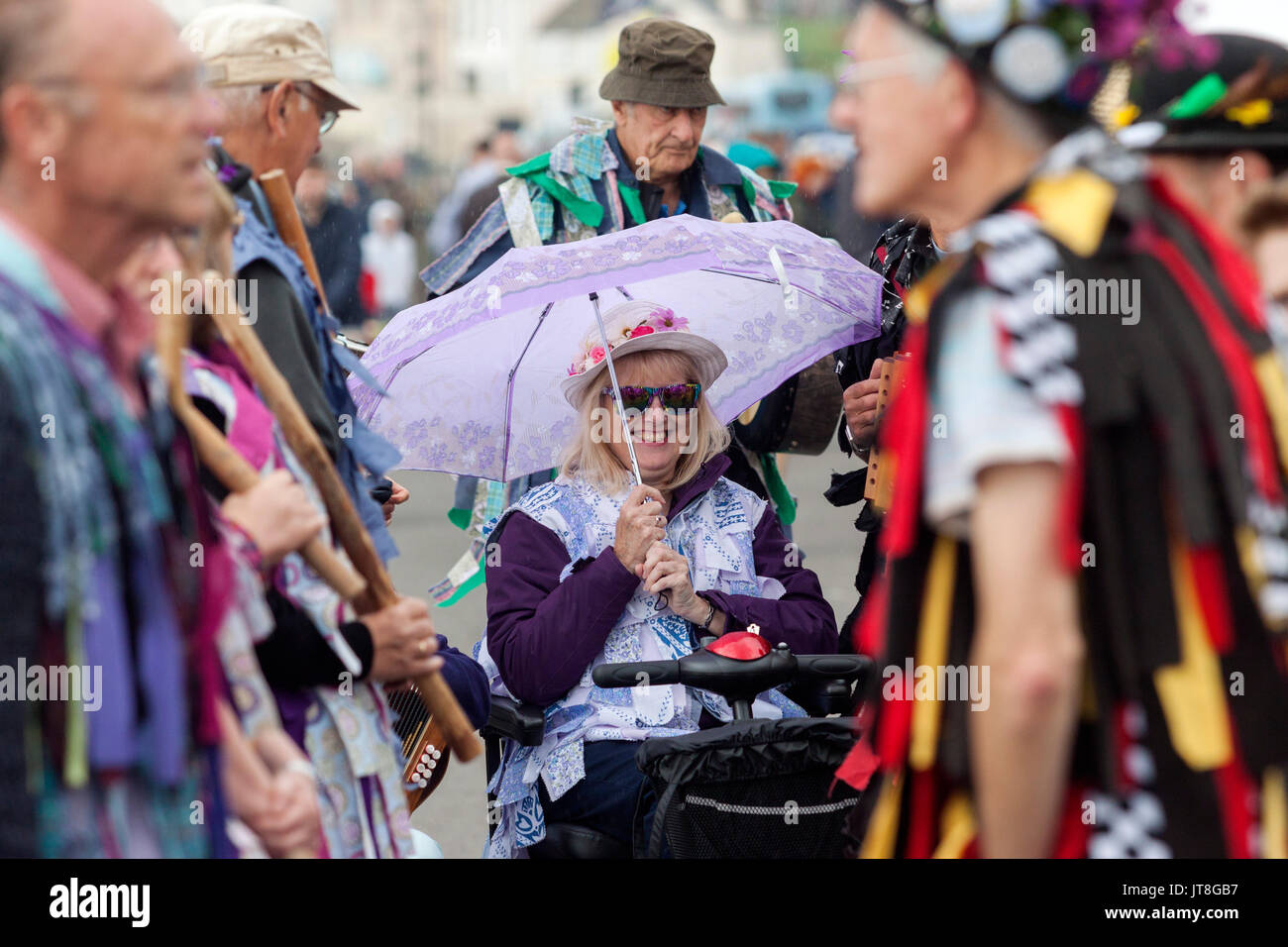 Sidmouth, 8 Agosto 17. Una signora ripari sotto un ombrello come ella attende una Morris Dance il display per avviare sulla spianata di Sidmouth durante la città annuale della settimana della musica folk festival. Tony credito Charnock/Alamy LiveNews Foto Stock