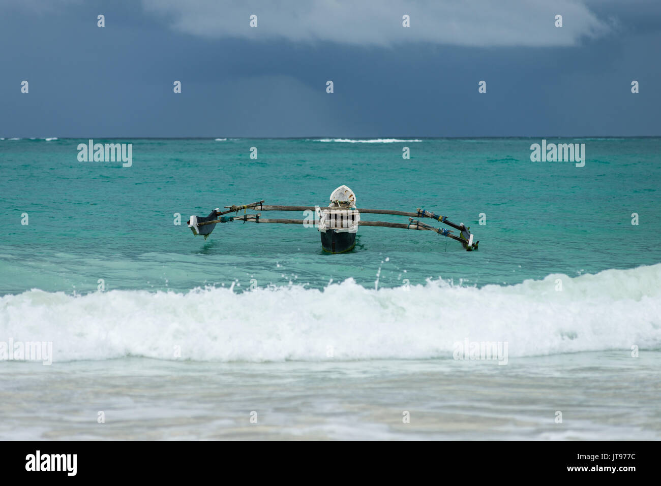 Un tradizionale dhow imbarcazione in legno ancorato sul litorale come surf breaks in primo piano e le nuvole scure in background oltre oceano Indiano, Diani, Kenya Foto Stock