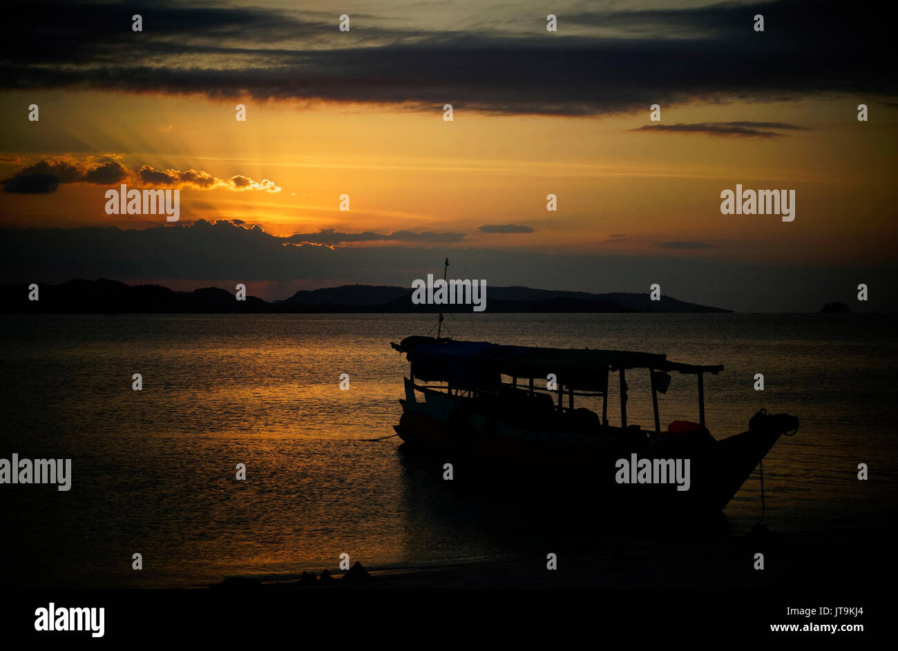 Silhouette della barca lunga sulla riva della spiaggia durante un golden arancione tramonto colorato in attesa di essere utilizzato come trasporto di diverse isole da a Foto Stock