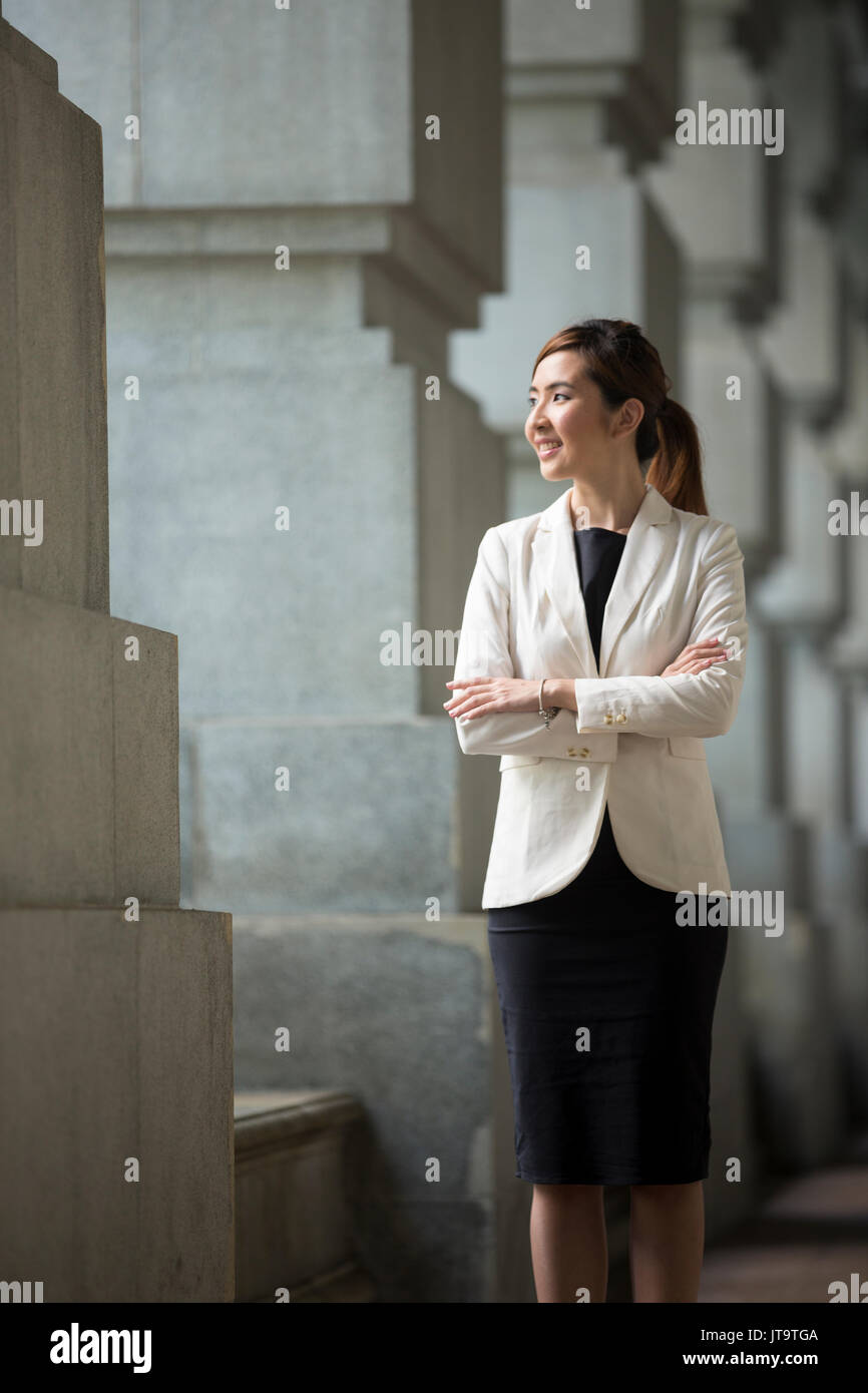 Asian business woman standing esterno con edifici per uffici in background. Ritratto di un cinese business donna guardando la telecamera. Foto Stock