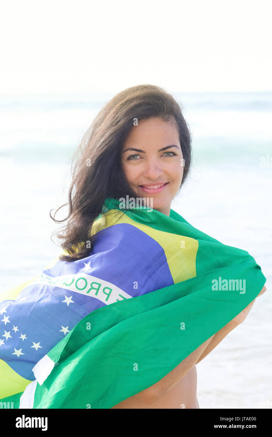 Giovane donna brasiliana 20 a 29 anni di età con una bandiera brasiliana beach avvolgere su una spiaggia, Rio de Janeiro, Brasile, Sud America Foto Stock