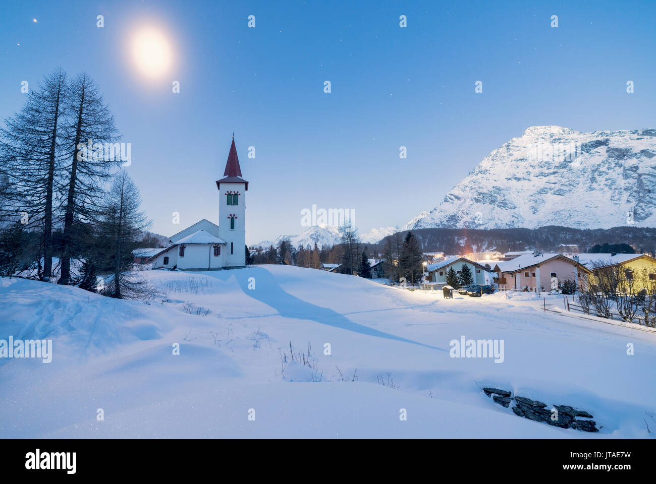 Luci del tramonto su Chiesa Bianca e il villaggio alpino coperto di neve, Maloja Pass, Engadina nel Cantone dei Grigioni, Svizzera, Europa Foto Stock