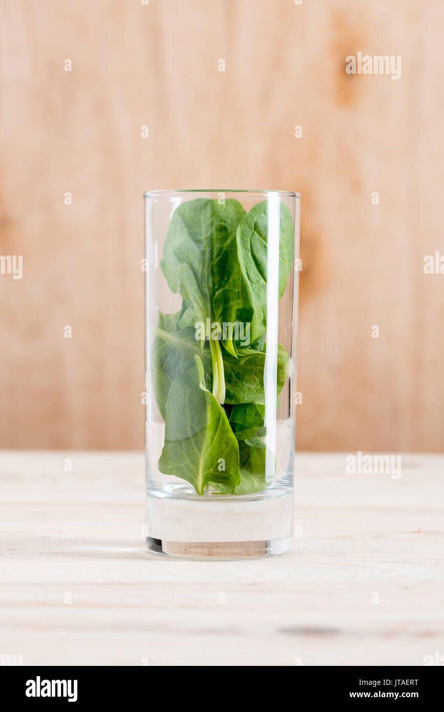Fresco Verde foglie di spinaci in vetro sul tavolo di legno, ingrediente per frullati Foto Stock