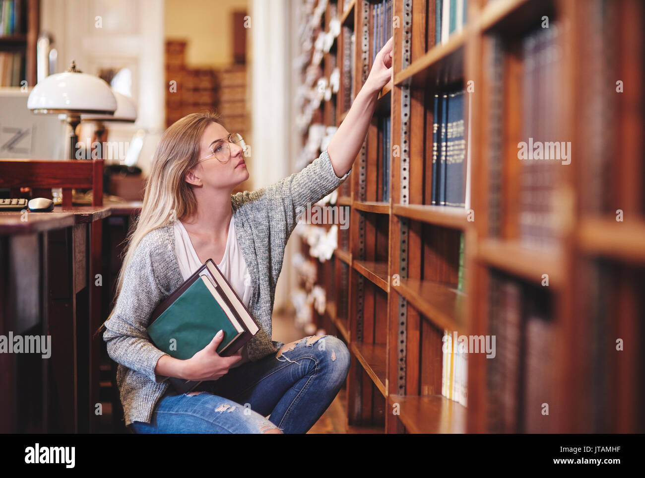 Donna di esaminare i libri in biblioteca Foto Stock