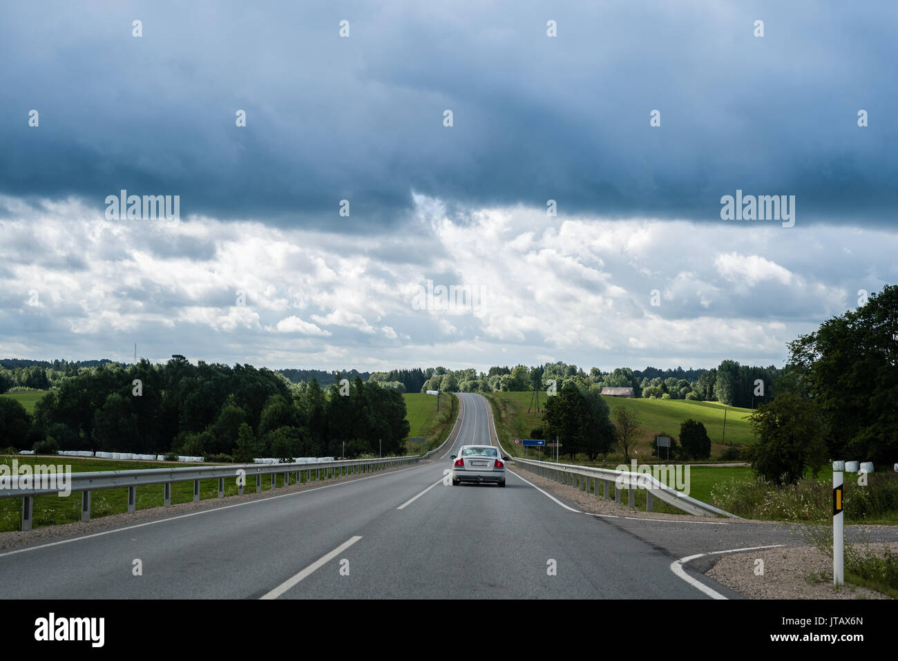 Automobile che si muove su per la collina sulla strada di campagna su nuvoloso giorno di estate in Lettonia Foto Stock