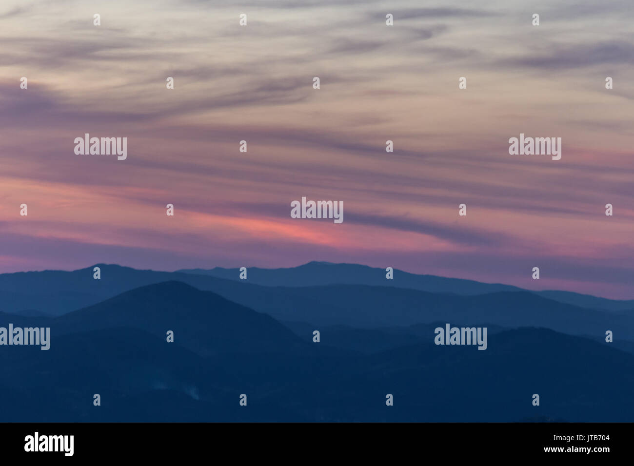 Bellissimo tramonto su alcune montagne con blu, viola e toni di rosso nel cielo, nuvole e colline Foto Stock