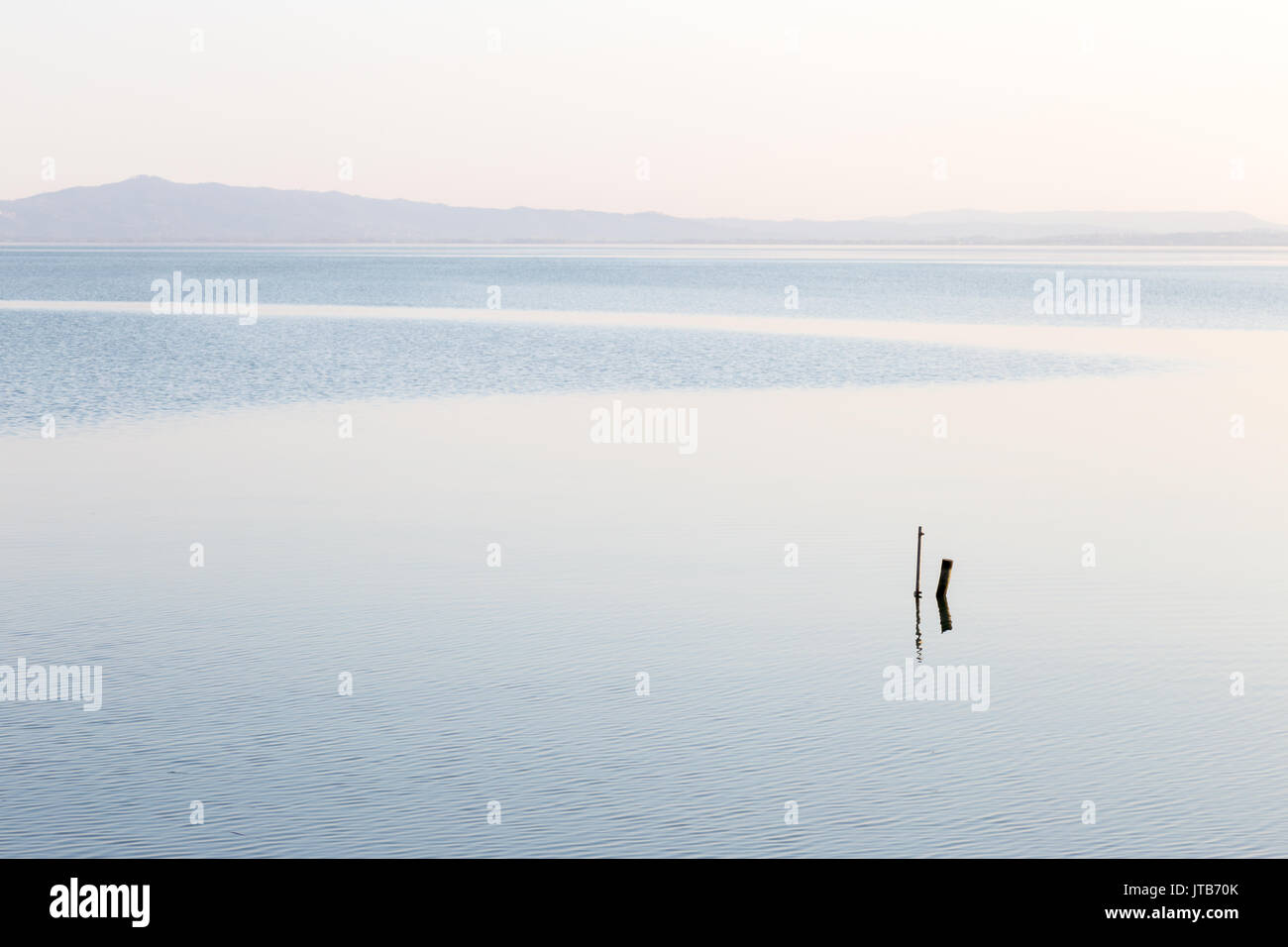 Mininalist vista di un lago, con alcuni pali di legno in primo piano e morbida, toni di blu Foto Stock