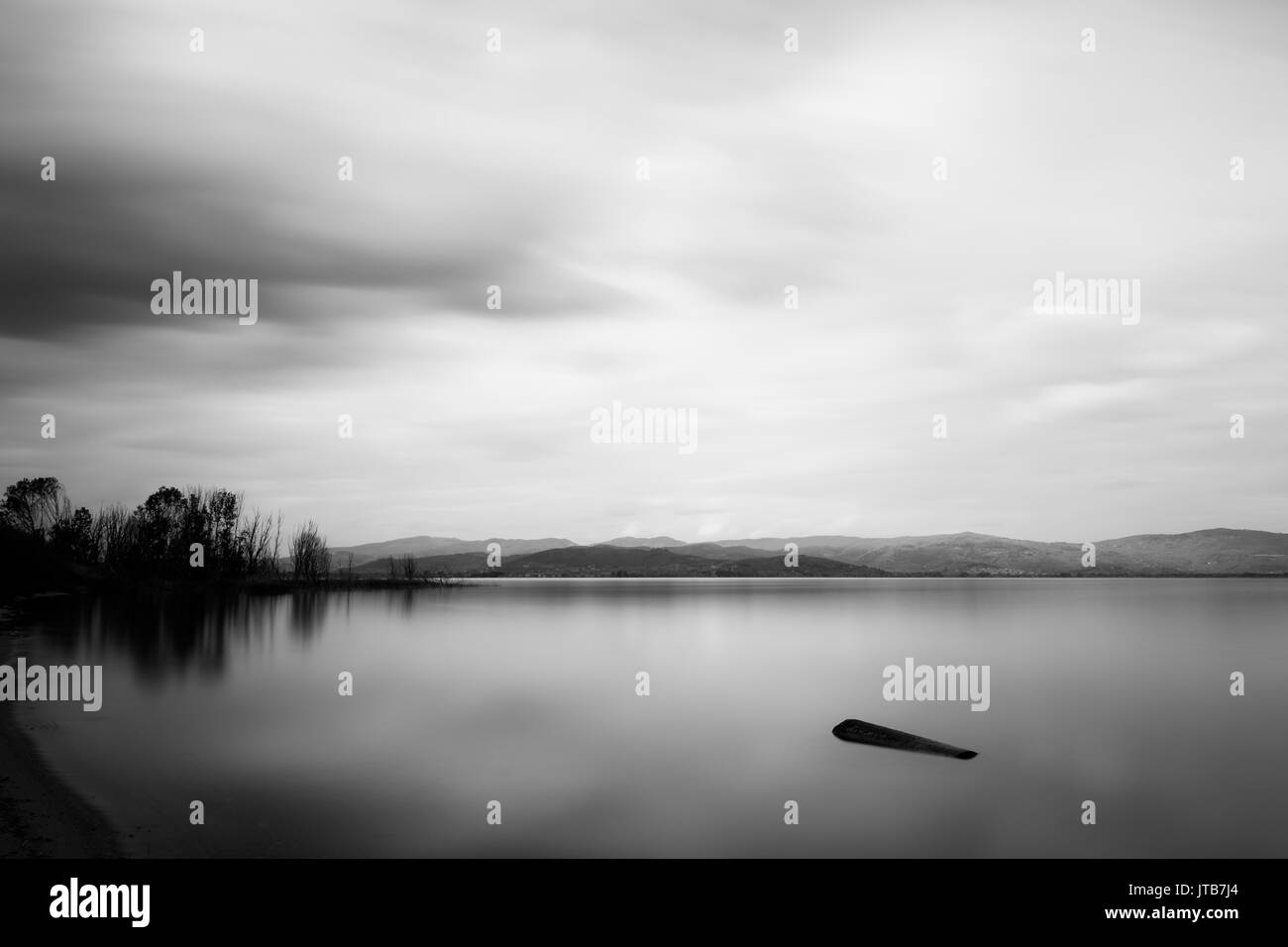 Un lago con un log in perfettamente ancora acqua e nuvole in movimento Foto Stock