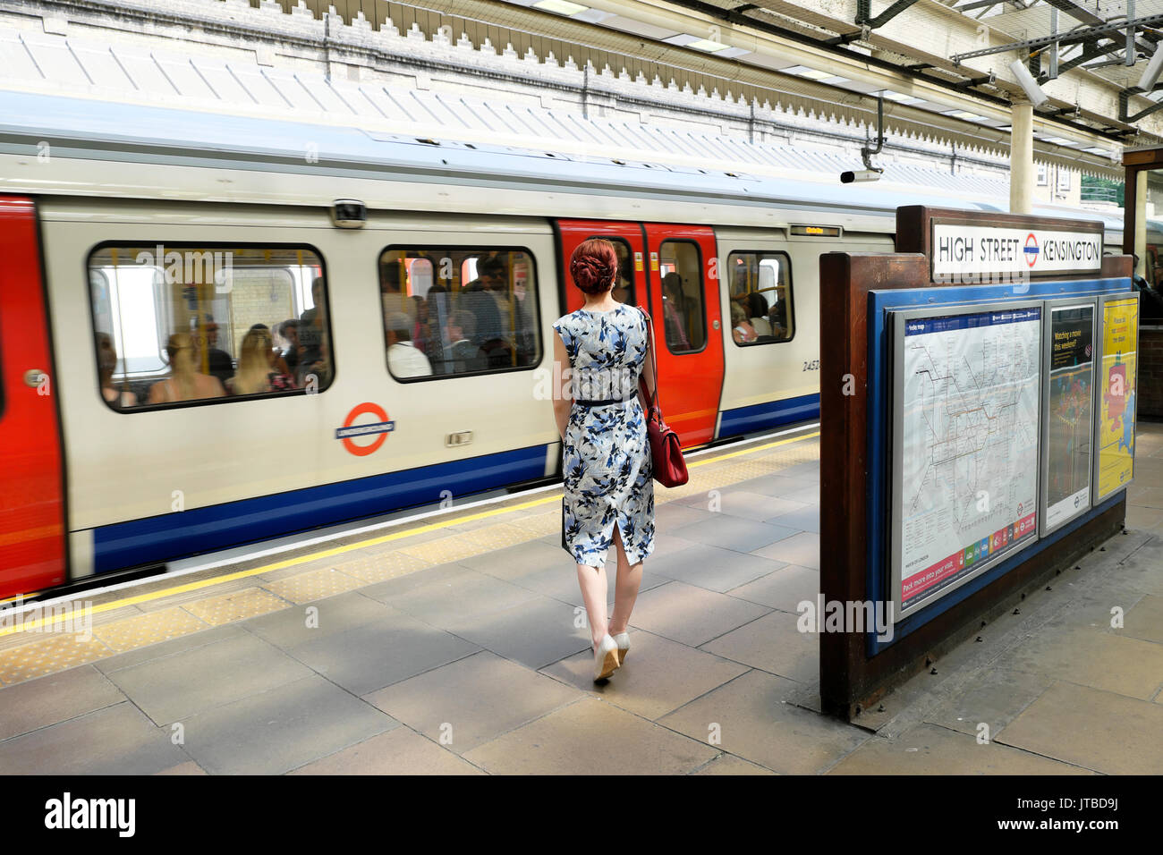 Vista posteriore di una donna attraente in abiti estivi in attesa sulla piattaforma a High Street Kensington metropolitana stazione della metropolitana di West London, Regno Unito KATHY DEWITT Foto Stock