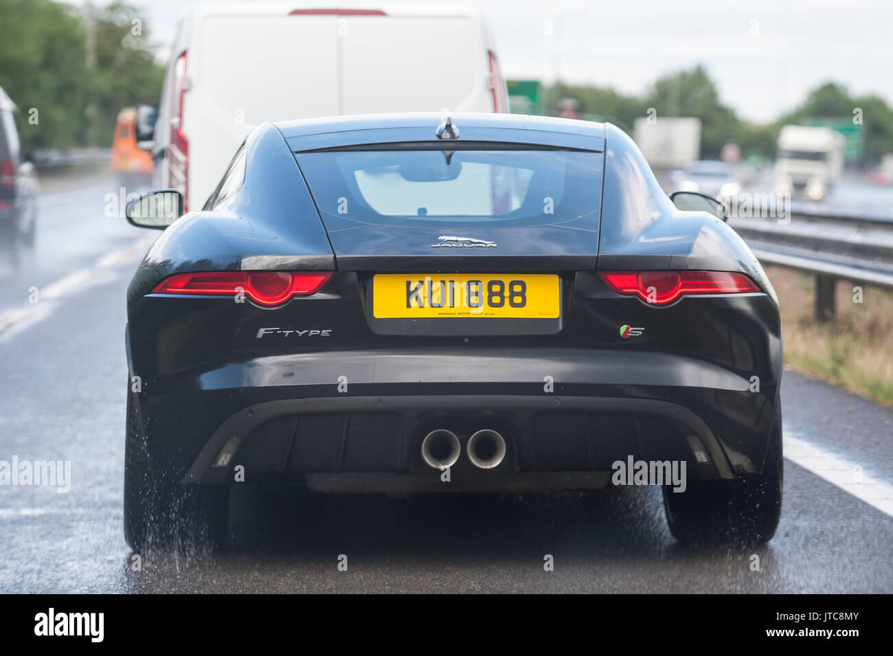Un Giaguaro Nero tipo F auto sportive guida sul bagnato su una strada principale nel Regno Unito Foto Stock