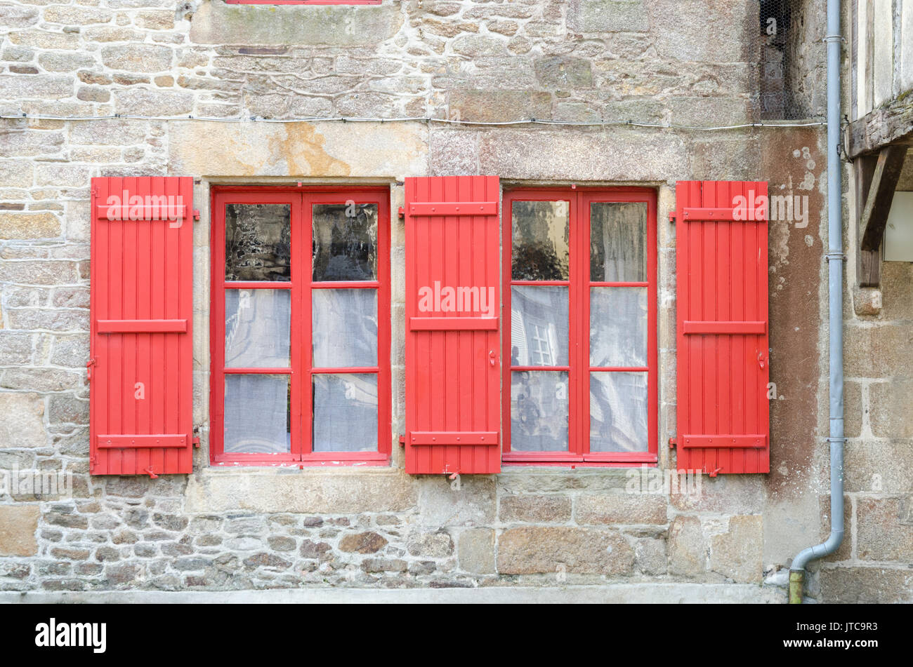 Red finestre e persiane rosse su una vecchia casa di pietra nella città murata di Dinan in Bretagna, Francia Foto Stock