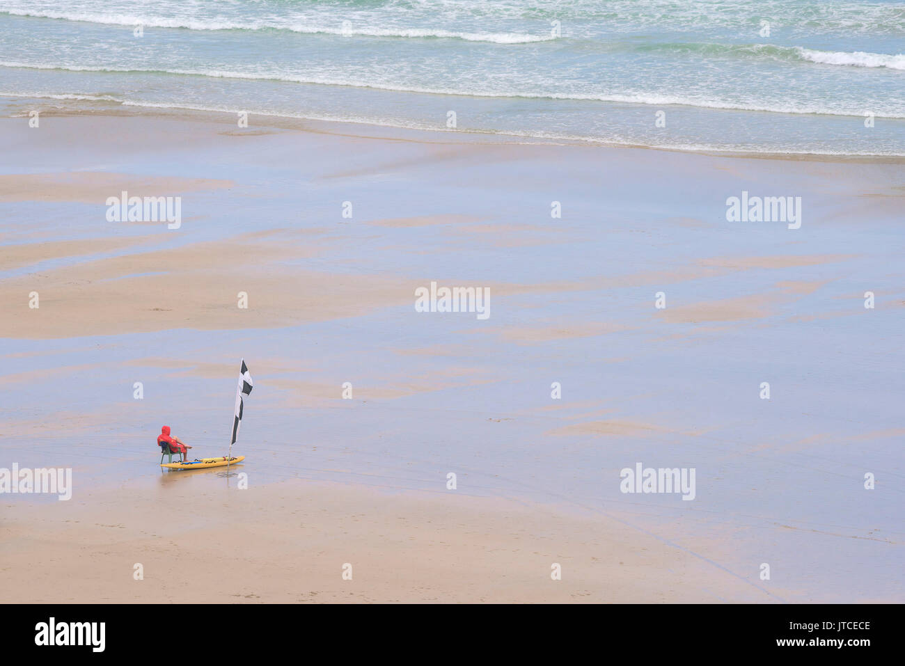 Un lone RNLI bagnino di turno su una tranquilla spiaggia deserta in Newquay, Cornwall. Foto Stock