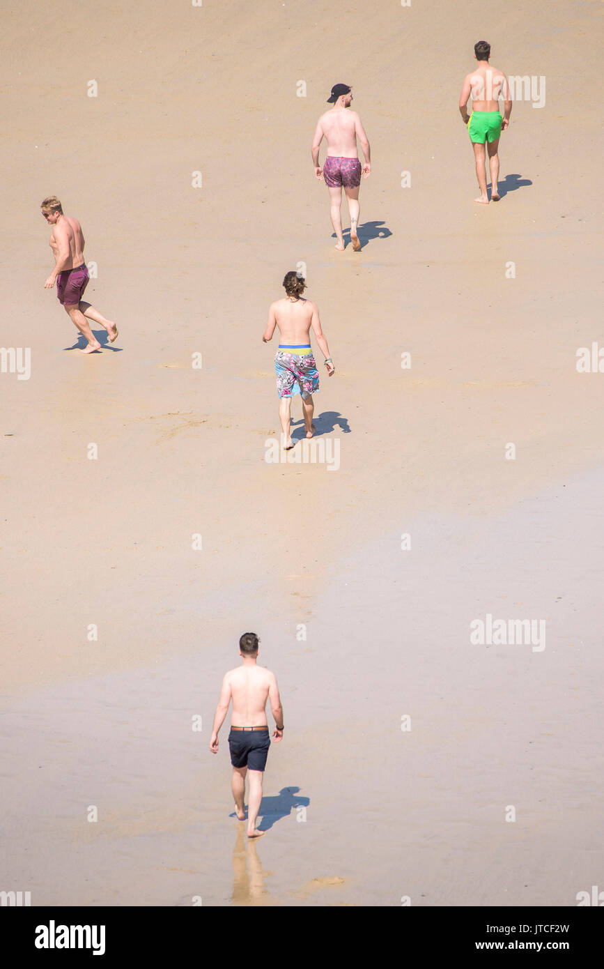 Cinque giovani uomini a piedi attraverso la Great Western Beach in Newquay, Cornwall. Foto Stock