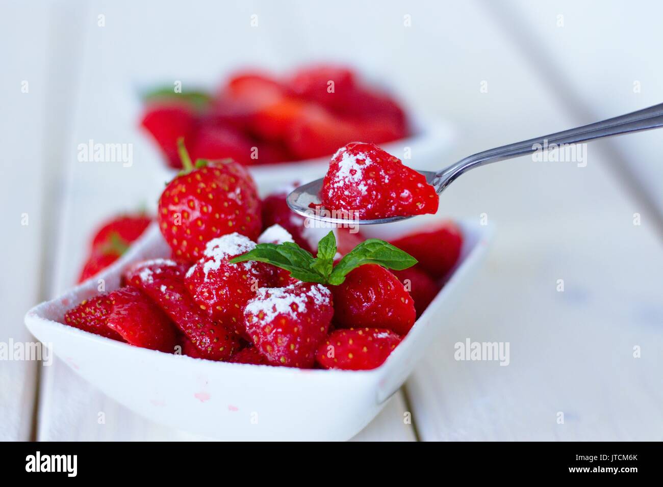 Cucchiaio di zucchero rivestite fresche fragole mature presi da una ciotola di frutta Foto Stock