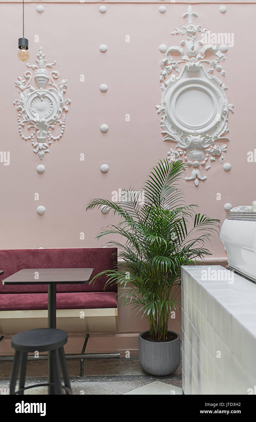 Ristorante con stucco bianco stampaggio sulla parete rosa e un pavimento piastrellato. Vi è un bianco piastrellate rack, piante verdi in vaso, divano rosso, nero tabella w Foto Stock
