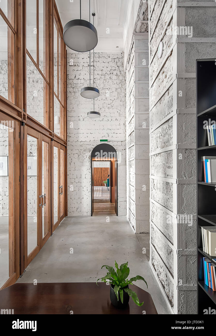 Interno in stile loft in cafe con luce shabby pareti e pavimento grigio. Vi è un tavolo di legno con un impianto, nero scaffali con libri, grande woo Foto Stock