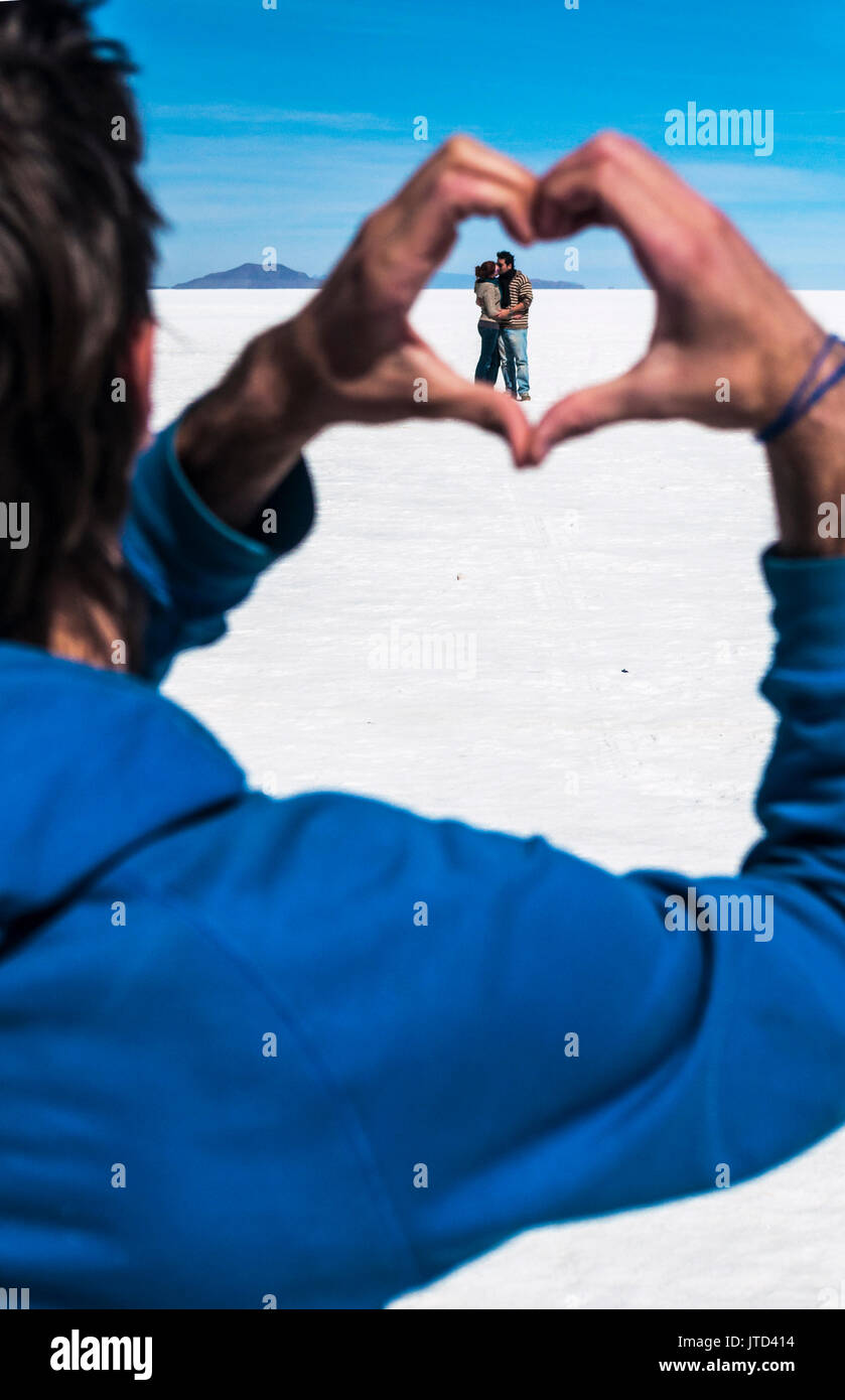 Un abbracciando giovane visto attraverso una forma di cuore realizzato unendo due mani, Uyuni Saline, Bolivia Foto Stock