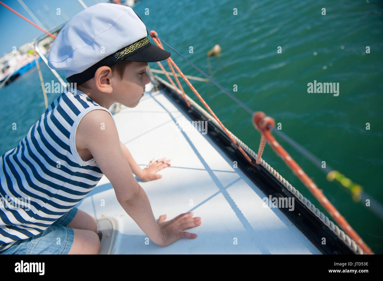 Curioso bello piccolo ragazzo in un capitano di hat peeking oltre il lato della barca Foto Stock