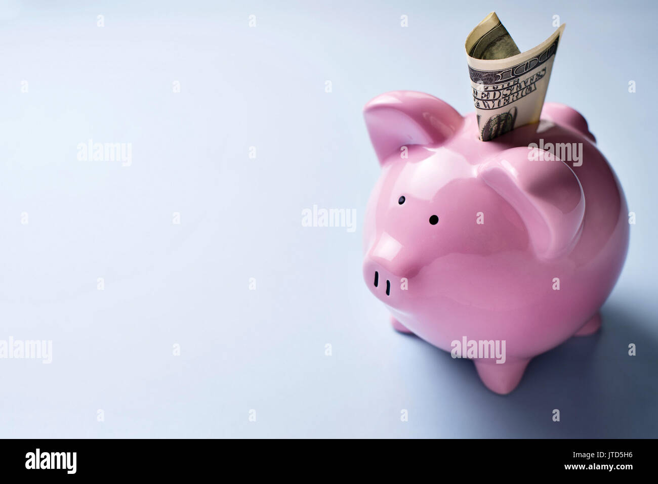 Angolo di alta vista di una ceramica rosa salvadanaio con un dollaro nella fessura sopra uno sfondo grigio con copyspace Foto Stock