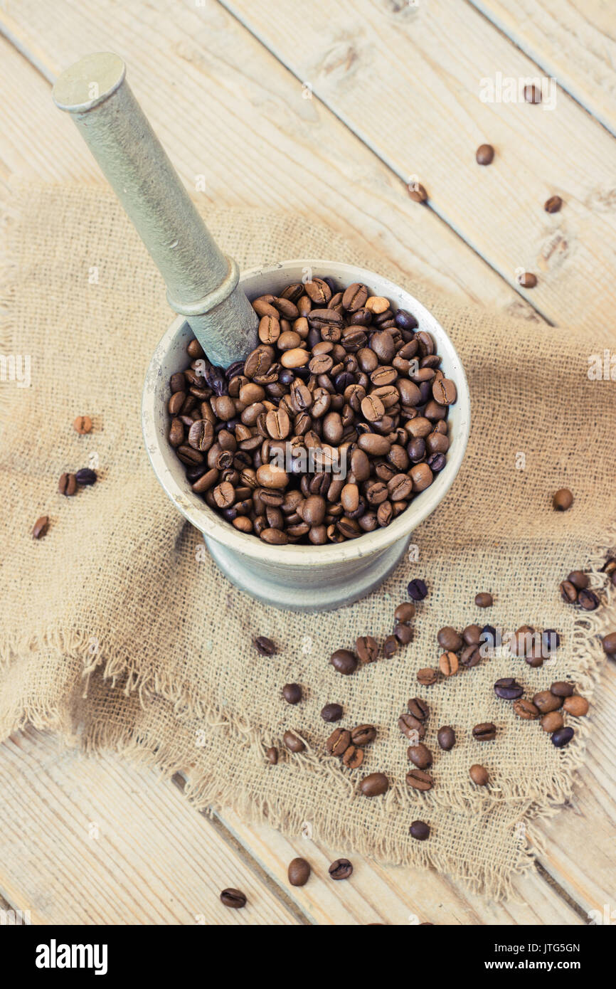 I chicchi di caffè in un mortaio di metallo su sfondo di legno tonificante Foto Stock