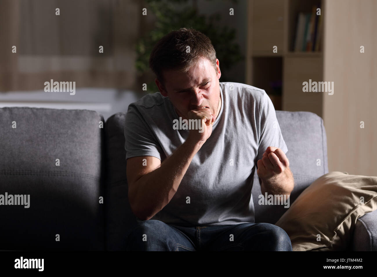 Vista anteriore verticale di un singolo uomo furioso a casa nel buio seduto su un divano a casa Foto Stock