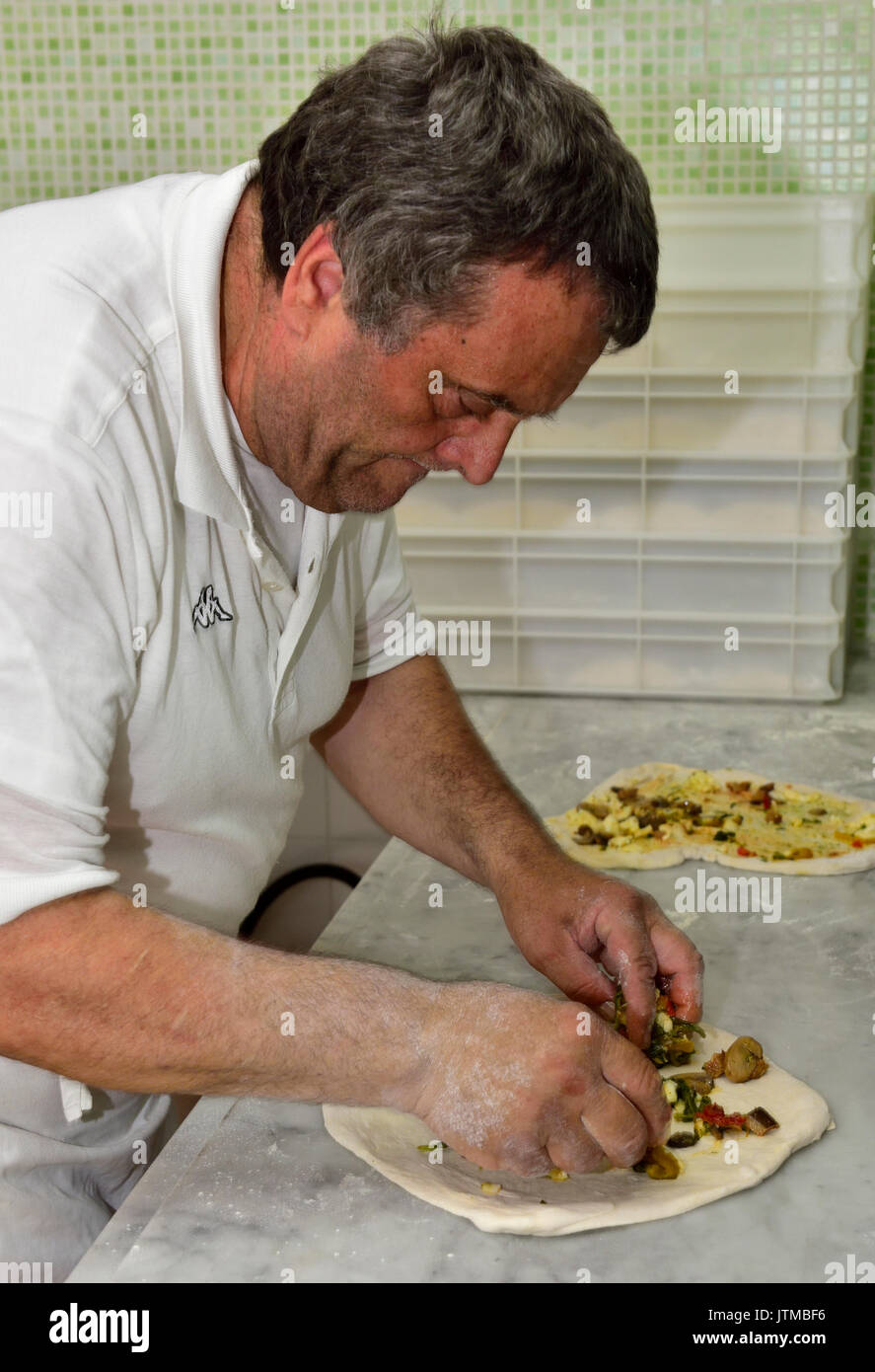 Chef italiani preparare la pizza aggiungendo gli ingredienti a base di pasta, Napoli, Italia Foto Stock