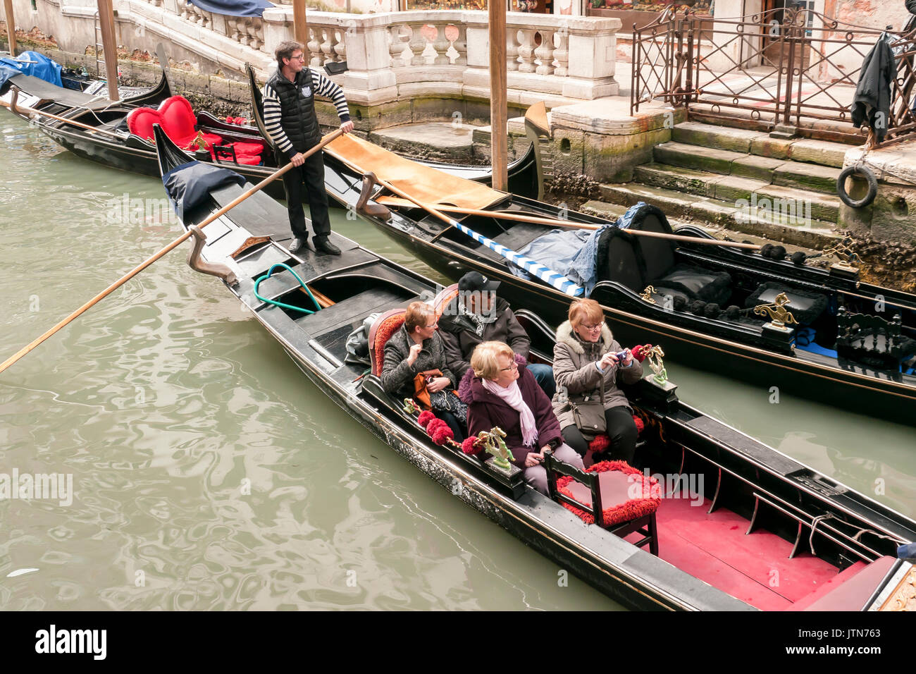 I turisti in una gondola con altre gondole ormeggiata in un canale di Venezia Foto Stock