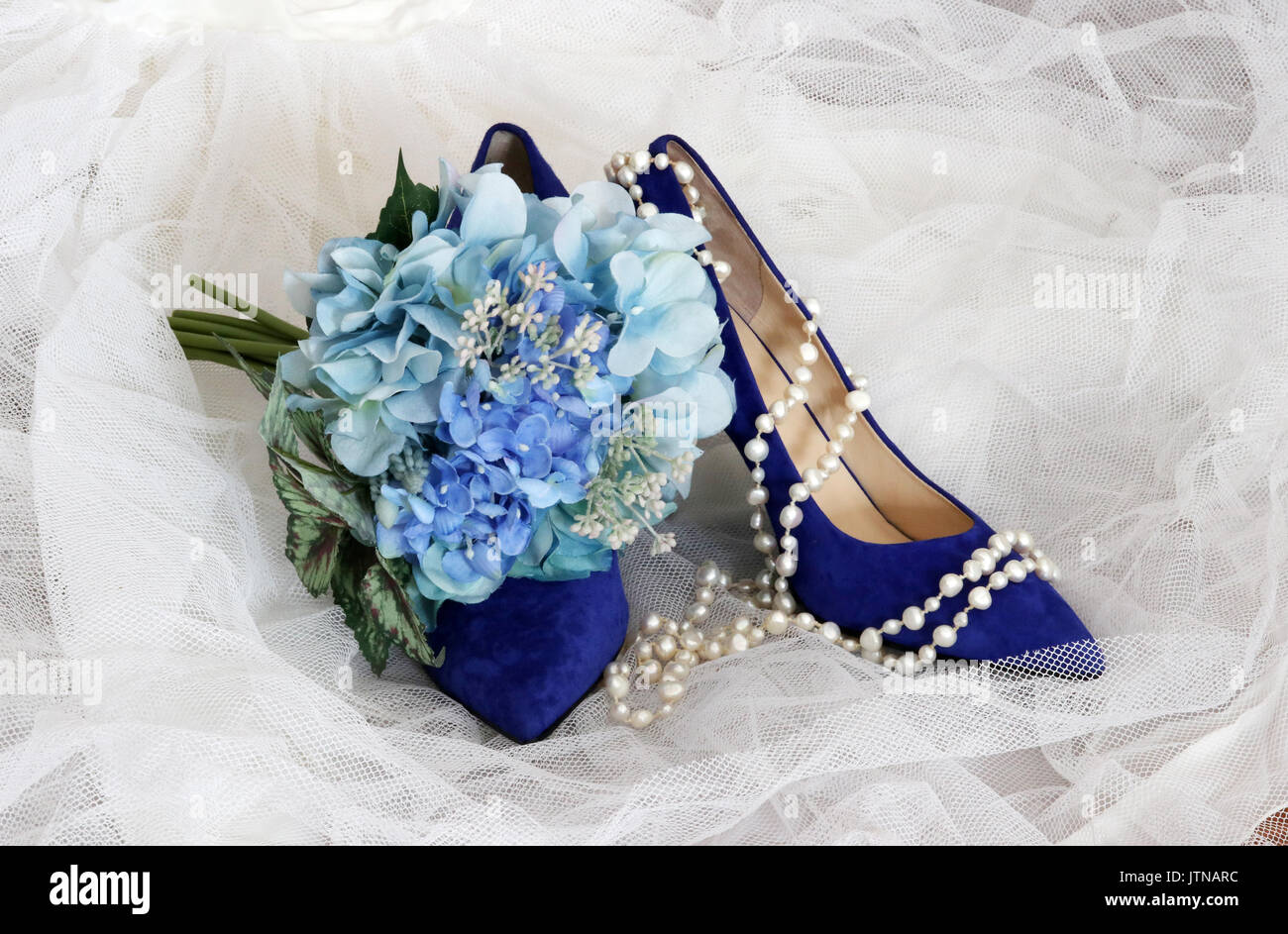 Lucido per Scarpe eleganti sposa. Bright blue suede alta collina paio di scarpe e spose bouquet con fiori blu su bianco velo nuziale. Foto Stock