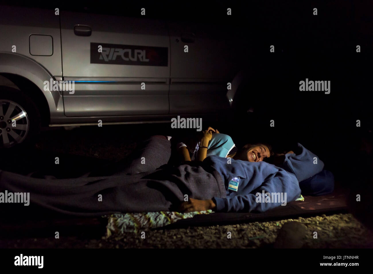 Giovane dormire vicino alla macchina di notte, Batukaras, Java, Indonesia Foto Stock