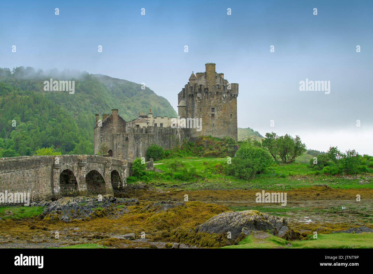 Vista della spettacolare Castello Eilean Donan e ponte sul loch contro il cielo blu e la nebbia in Scozia Foto Stock