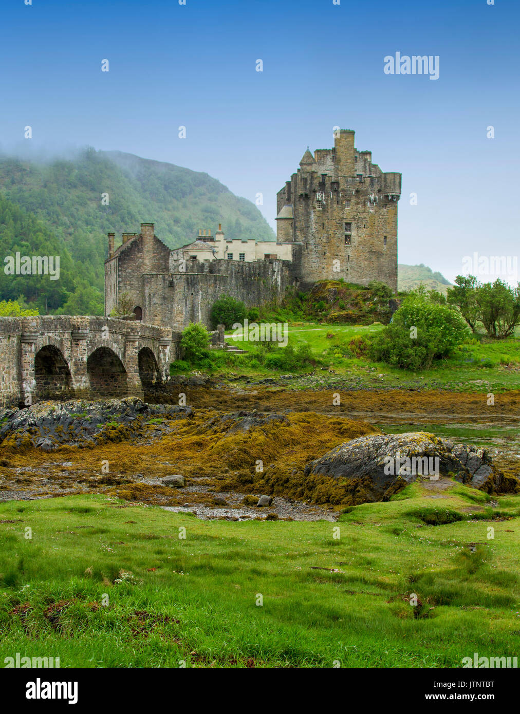 Vista della spettacolare Castello Eilean Donan e ponte sul loch contro il cielo blu e la nebbia in Scozia Foto Stock