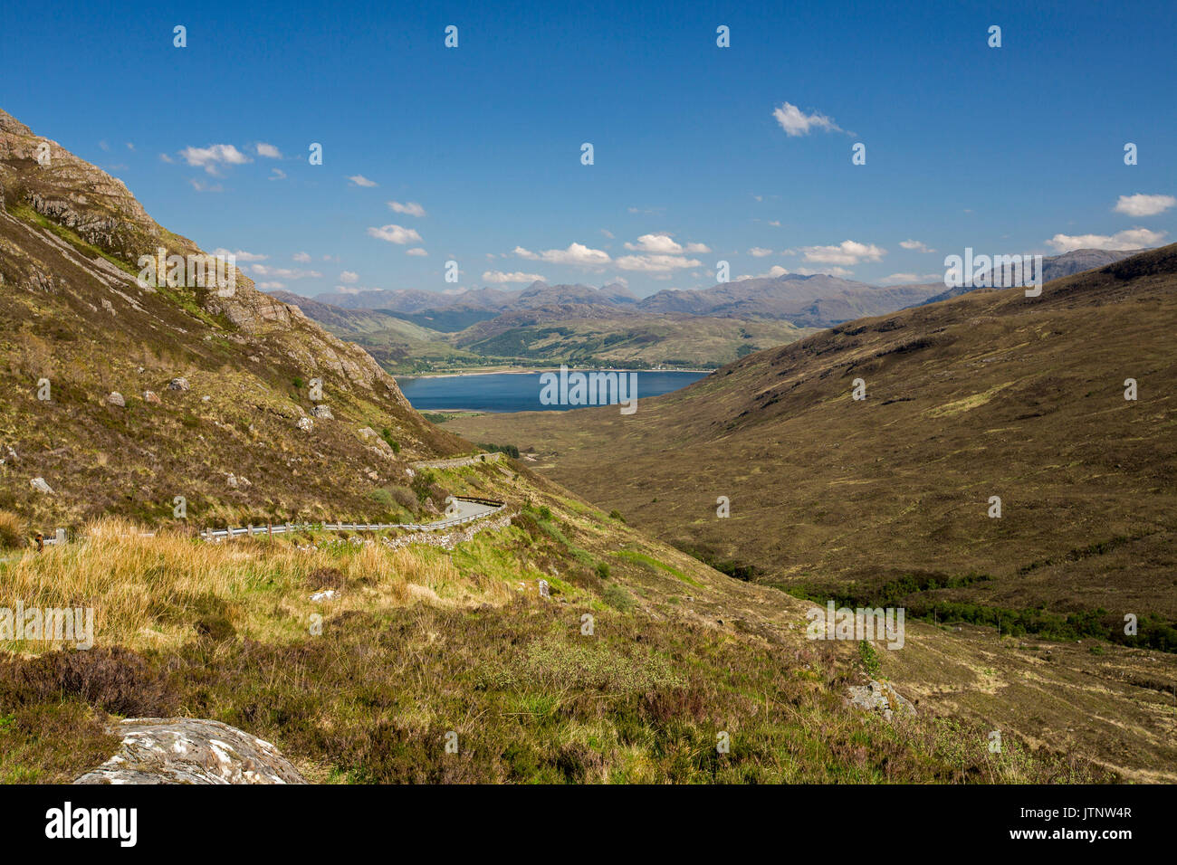 Spettacolare vista lungo la strada per Kylerhea sull isola di Skye, con montagne di terraferma scozzese di distanza al di là di acque blu dell'oceano sotto il cielo blu Foto Stock