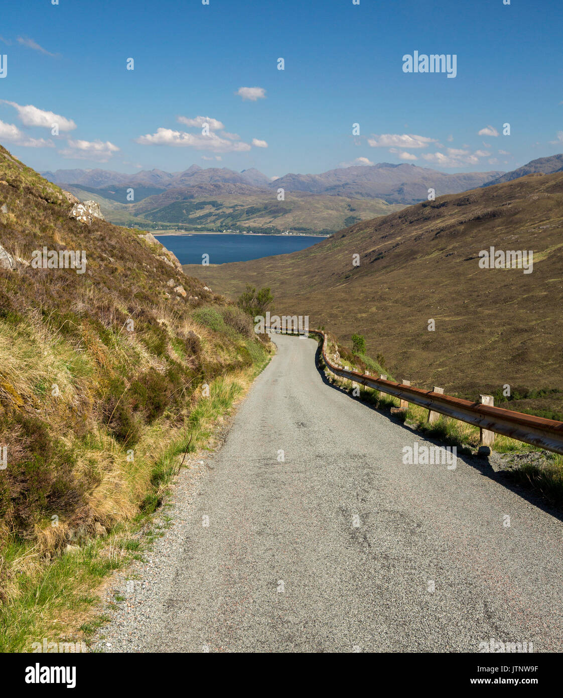 Spettacolare vista lungo la strada per Kylerhea sull isola di Skye, con montagne di terraferma scozzese di distanza al di là di acque blu dell'oceano sotto il cielo blu Foto Stock