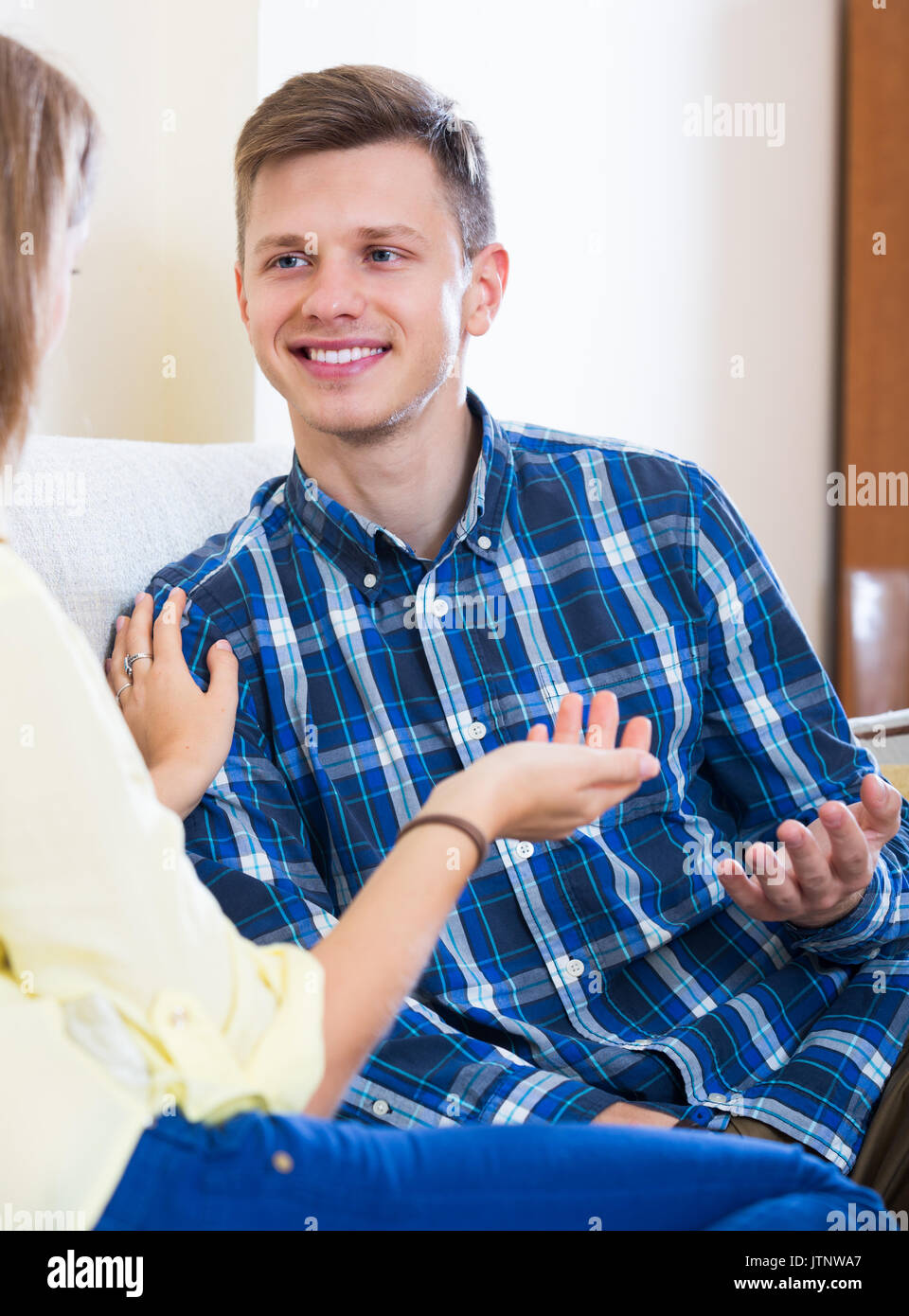 Allegro giovane ragazzo avente la conversazione positiva con la sua fidanzata in ambienti interni Foto Stock