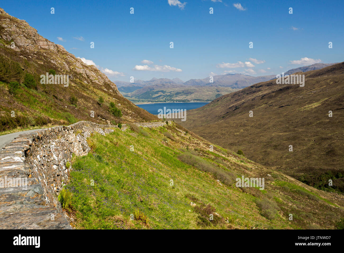 Spettacolare vista lungo la strada per Kylerhea sull isola di Skye, con montagne di terraferma scozzese di distanza al di là di acque blu dell'oceano sotto il cielo blu Foto Stock