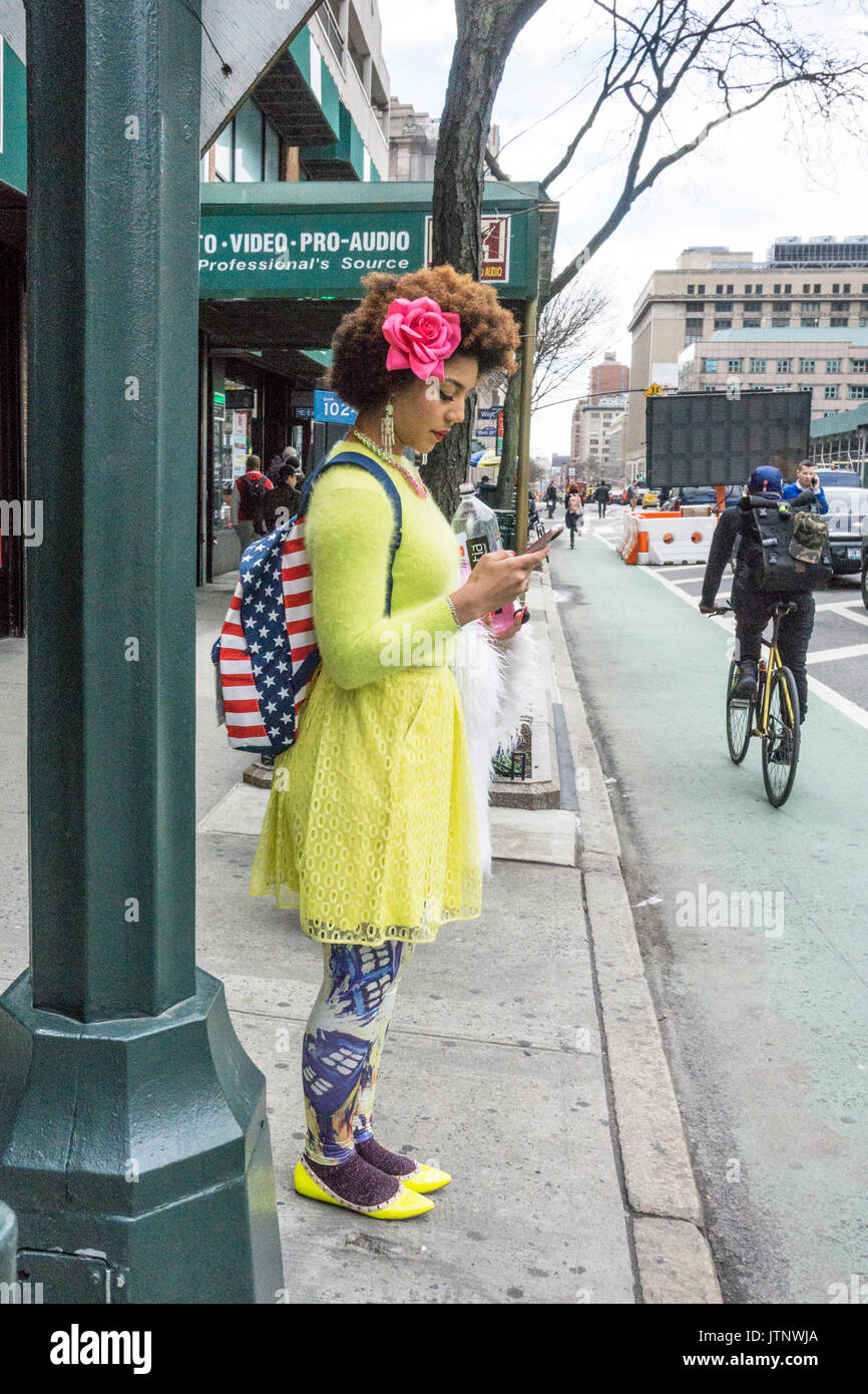 Deliziosa giovane fashionista indossando faux rose nel suo afro, un daffodil maglione colorato mantello & Scarpe, Stars & Stripes zaino, wild collant stampati Foto Stock