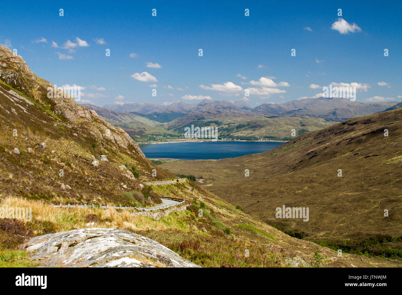Spettacolare vista lungo la strada per Kylerhea sull isola di Skye, con montagne di terraferma scozzese di distanza al di là di acque blu dell'oceano sotto il cielo blu Foto Stock